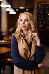 Beautiful attractive cute serious girl blonde freelancer sitting drinking coffee, working, talking on the phone, reading a newspaper in a cozy coffee shop in the loft style , portrait of a businesswom