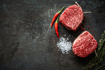 Two juicy filet Mignon beef steaks prepared for grilling with spices and herbs, top view and copy space