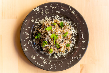 above view of fresh homemade italian mushroom risotto on wooden table with soft natural light with parmesan cheese and parsley leaves
