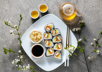 vegan sushi with tofu in General Tso sauce, avocado and fresh vegetables . on a table with branches of a blossoming tree and green tea in a glass teapot
