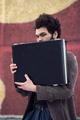 Curly man holding a suitcase and looking at the camera.