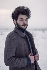Handsome bearded man in a coat in a winter field.