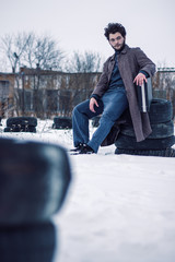 Handsome bearded man in a coat sits on tires.