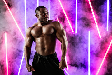 Athlete African American muscular man in smoke on a background of neon lamps