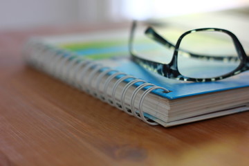 spectacles on diary on brown wood table .