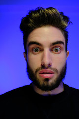 Beautiful caucasian young man portrait isolated on multicolored neon light backgroud. Young, smiling, surprised, screaming. Human emotions, facial expression concept. Trendy colors.Advertising concept