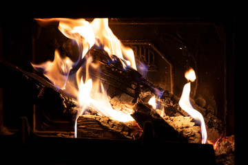 Fire in fireplace close up. Flames burning with wood logs in fire place. Cozy scene, with yellow and orange flares.
