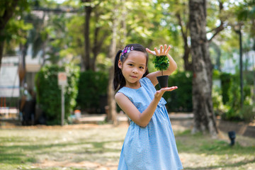 little girl holding small artificial plant in a garden