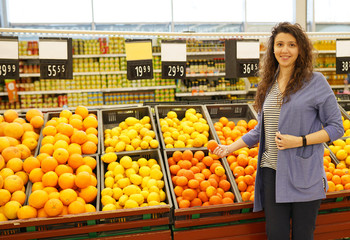 Beautiful woman standing in supermarket near citrus fruits. Female customer choosing citruses products.