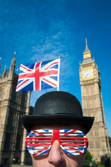 Patriotic British politician wearing a traditional bowler hat with a Union Jack flag and glasses standing in front of the Houses of Parliament at Westminster, London, UK