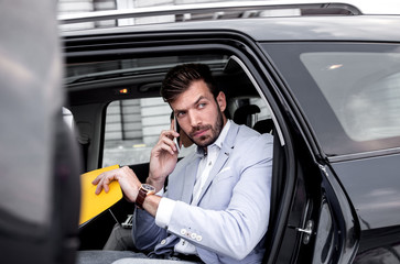 Young businessman talking on phone while he enters the car.