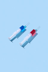 Disposable syringes of red and blue vaccine with shadows.