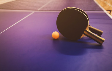 Two table tennis or ping pong rackets and balls on a blue table with net