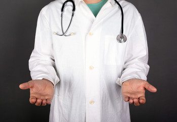 doctor in a white coat with a stastoscope on a dark background stretch out hands and palms copy space