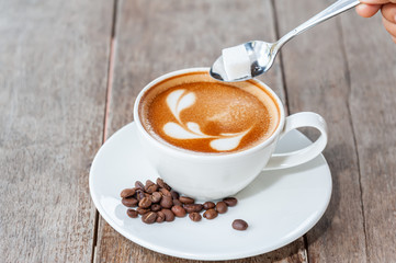 Hand with spoon put sugar of coffee, Hot coffee in white cup on table 