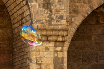 A rainbow-colored soap bubble flies against the background of an ancient masonry wall.