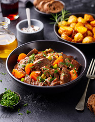 Beef meat and vegetables stew in black bowl with roasted baby potatoes. Dark background. - 328039113