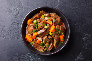 Beef meat and vegetables stew in black bowl. Slate background. Top view. - 328039515