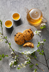 homemade oatmeal cookies on a table with branches of a blossoming tree and green tea in a glass teapot.