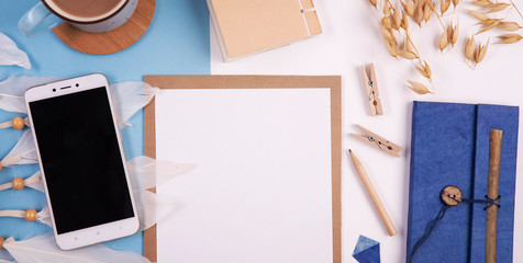Blank frame of paper with wooden pencil, clips, and empty smartphone on office desk. Business and technology on blue table for work. Top view and panoramic.
