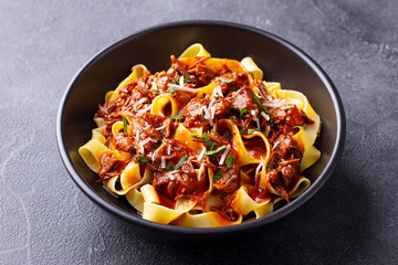 Pasta pappardelle with beef ragout sauce in black bowl. Grey background. Close up.
