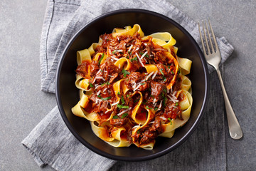 Pasta pappardelle with beef ragout sauce in black bowl. Grey background. Top view. - 328040336