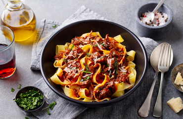 Pasta fettuccine with beef ragout sauce in black bowl. Grey background. Close up.