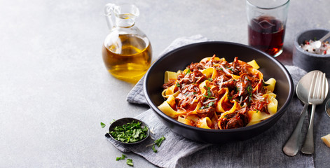 Pasta pappardelle with beef ragout sauce in black bowl. Grey background. Copy space.