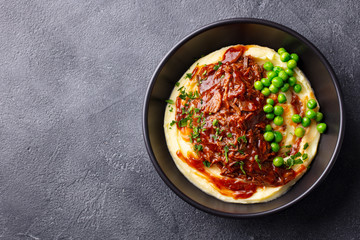 Mashed potatoes with beef meat and green peas in bowl. Dark background. Copy space. Top view.