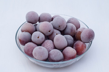 Frozen plums in a glass bowl on a white wooden background. Frozen fruits.