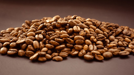 Background from a dense layer of brown roasted coffee. Fresh fragrant dark grains for bitter drink.