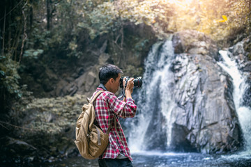 Tourists man or photographer in backpacks standing and holding a camera for taking a photo nature in forest.