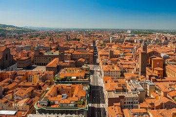 Fototapeta premium Panoramic aerial view of the old Bologna city, with terracotta houses and regular roofs with central square Piazza Maggiore and main street with blue sky over horizon.