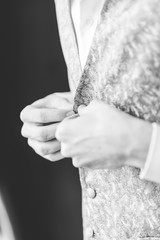 A groom putting on cuff-links as he gets dressed in formal wear .
