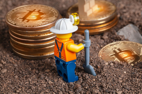 ANKARA, TURKEY. NOVEMBER 17, 2019. Lego mini miner figurine with shovel standing near bitcoin piles on ground. Cryptocurrency, blockchain and mining concept.