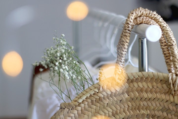 Round straw bag and capsule wardrobe in white and neutral colors. Selective focus, bokeh lights in the foreground.