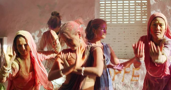 Women dancing celebrating Holi festival in India, joined by their male friends as they do traditional ceremonial dance as one guy beats a local drum with stick for beats, they enjoy have fun good time