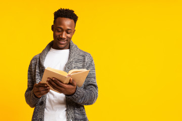 Romantic african guy reading poetry in old book on yellow - obrazy, fototapety, plakaty