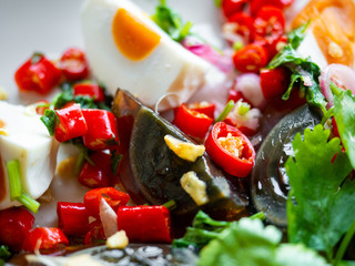 Salted egg and Century egg salad Thai food menu,Spicy, sour, salty, sweet taste. Main ingredients,Salted egg and Century eggs. Onion, Coriander, Lime, Chili, Onion on a white plate. Black background.