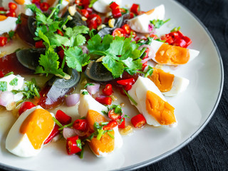 Salted egg and Century egg salad Thai food menu,Spicy, sour, salty, sweet taste. Main ingredients,Salted egg and Century eggs. Onion, Coriander, Lime, Chili, Onion on a white plate. Black background.