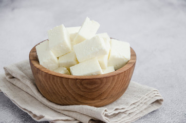 Homemade Indian paneer cheese made from fresh milk and lemon juice, diced in a wooden bowl on a gray stone background. Horizontal orientation. Close up.