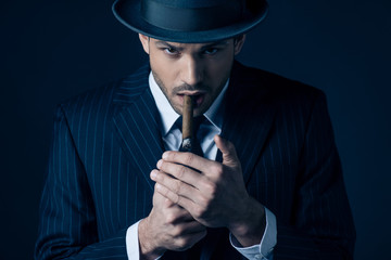 Mafioso lighting cigar and looking at camera on dark background