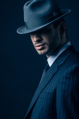 Fototapeta na wymiar Mafioso in suit and felt hat on dark blue background