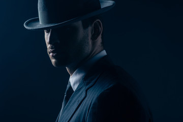 Portrait of mafioso in felt hat and suit on dark blue background