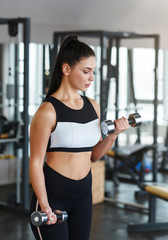 Fototapeta premium Young woman with dumbbells on her workout in gym