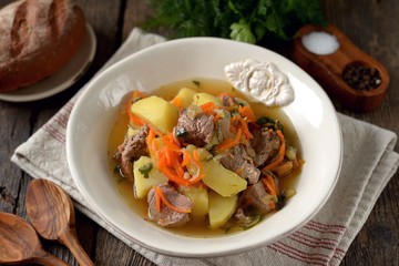 Beef stew with potatoes, onions and carrots on a wooden background.