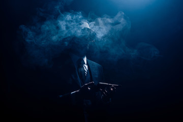 Silhouette of gangster holding gun and smoking on dark background