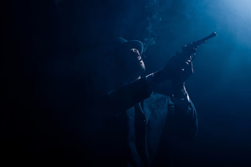 Fototapeta na wymiar Silhouette of gangster aiming revolver and smoking on dark background
