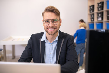 Fototapeta na wymiar Male teacher sitting at laptop, wearing eyeglasses, smiling