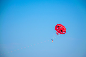 Two persons flying with a red sea parachute against the blue sky